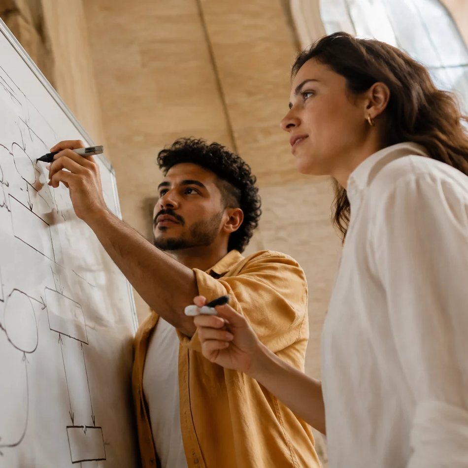 Duas participantes de pé junto ao quadro branco, desenhando as partes de um argumento
